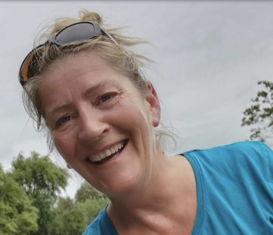 Een lachende vrouw met zonnebril op haar hoofd, buiten naar de camera kijkend.
