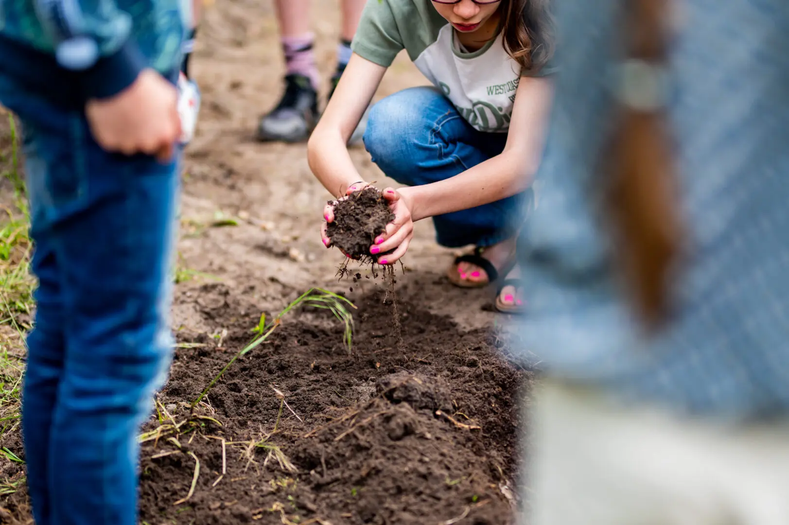 Child planting seeds in soil with others nearby, highlighting gardening activity.
