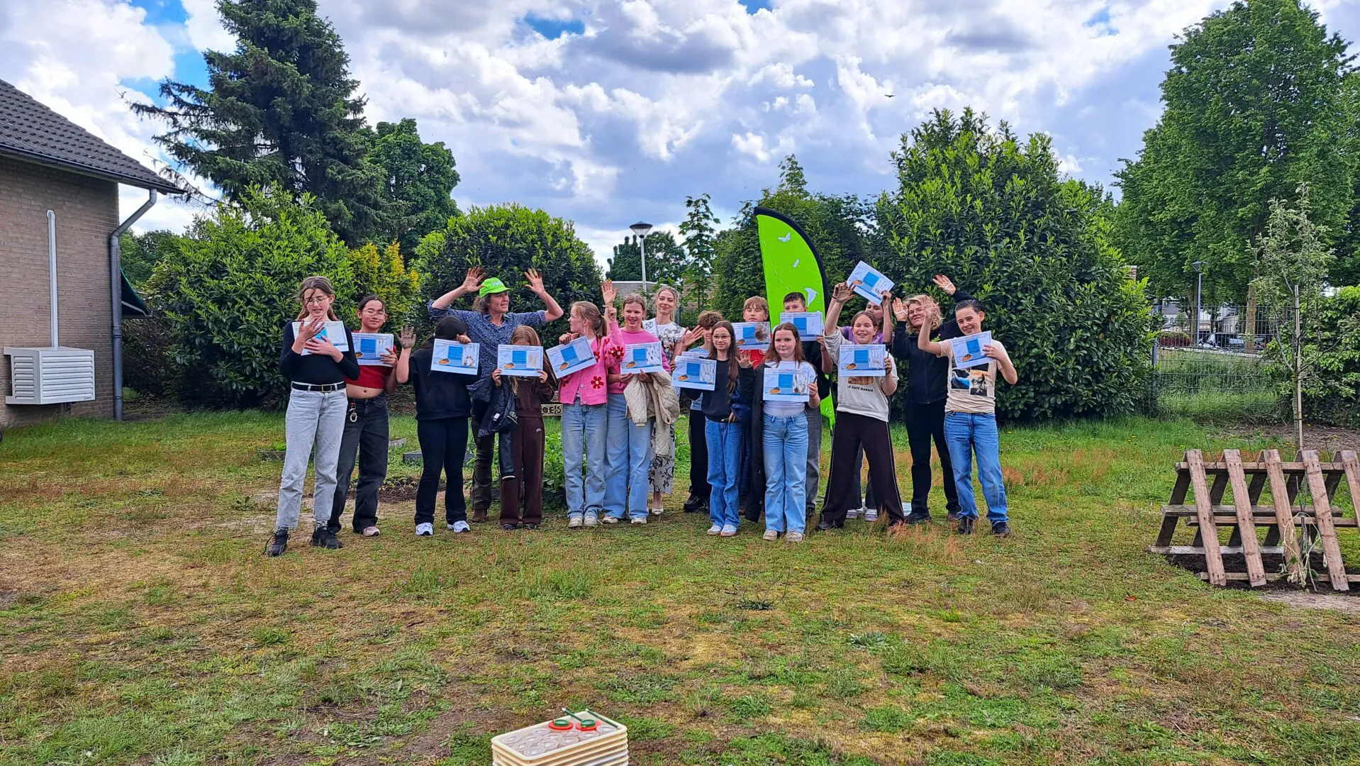 Groep mensen viert buiten, anderen tonen certificaten. Groene achtergrond met bomen.