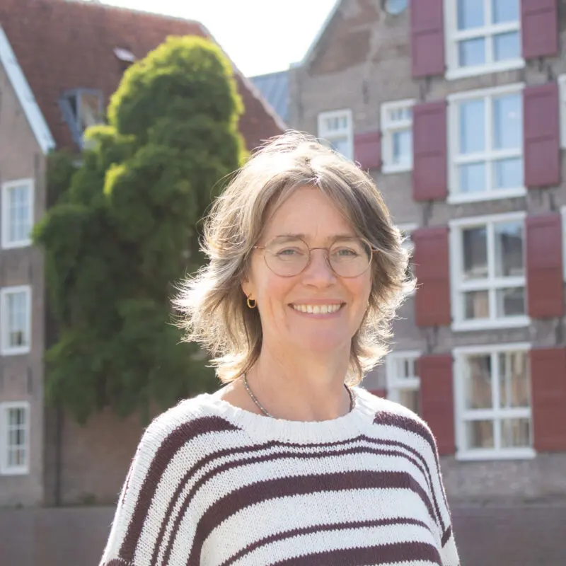 Persoon met bril en gestreepte trui voor oude bakstenen huizen met rode luiken.