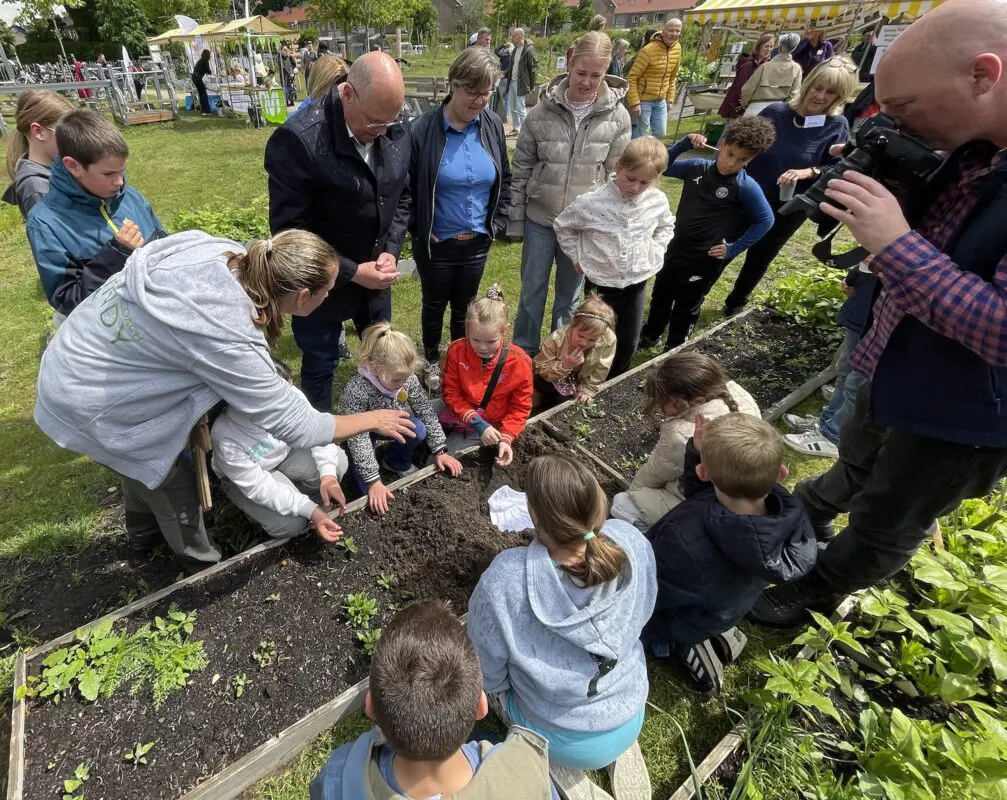 Kinderen leren tuinieren in een moestuin onder begeleiding van volwassenen op een zonnige dag.